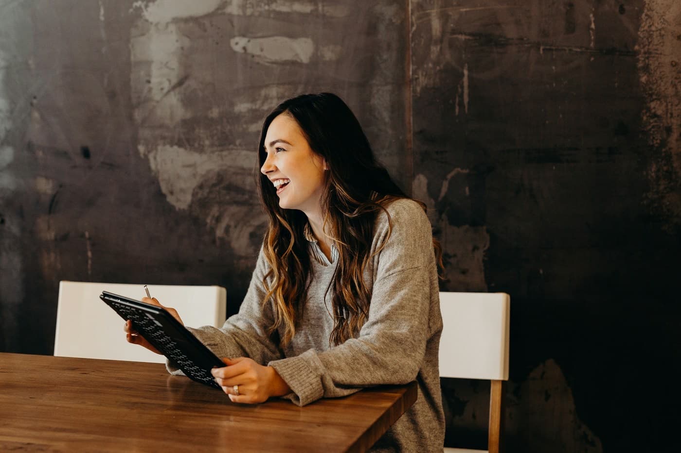 Mulher sorrindo com um tablet nas mãos, sentada à mesa