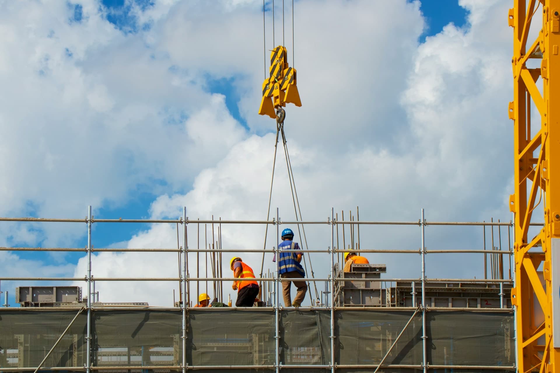 Equipe de operários com capacete e colete trabalhando no alto de uma obra, com grua ao fundo
