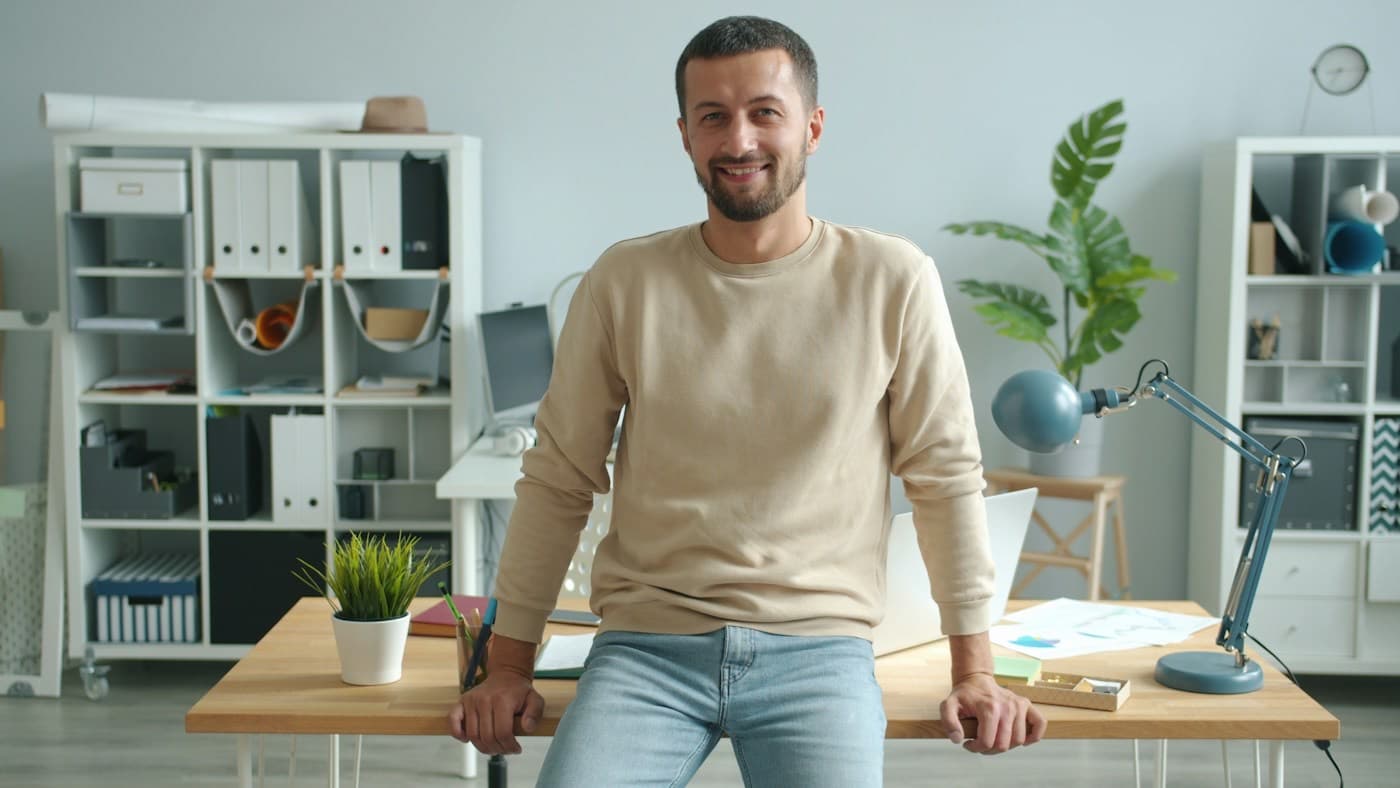 Empresário sorrindo, apoiado na mesa do seu escritório